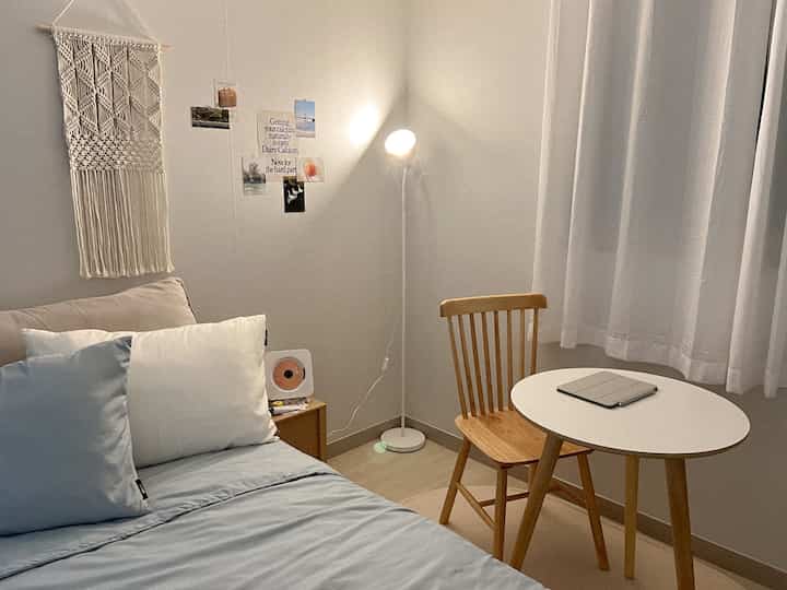 白と青のトーンが印象的な寝室、木製チェアと小さな丸テーブルが配置された雰囲気のあるインテリア