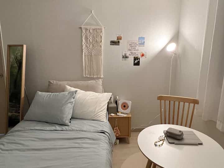Natural modern small bedroom with white and wood tones featuring a single bed, round table, nightstand, and floor lamp in a cozy layout
