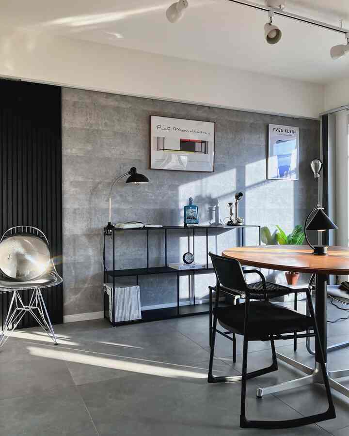 グレーのコンクリート壁に木製の丸テーブルと黒い椅子が配置されたインダストリアルスタイルのダイニングルーム