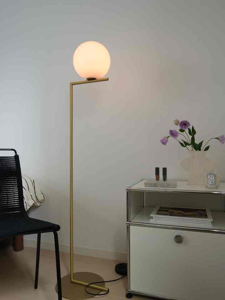 Nordic style bedroom in white and beige tones featuring a gold floor lamp and a vase with flowers, in a simple setting