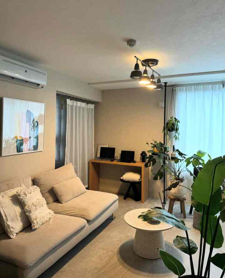 Beige and natural toned living room featuring a 3-person sofa, wooden desk, and lush plants with a bright, cozy atmosphere