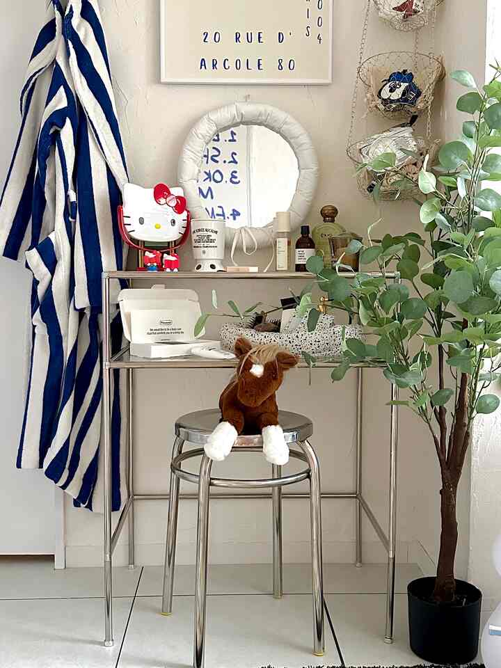 シルバーと白を基調とした狭い空間、ステンレス製スツールとメタルシェルフ、植物と鏡が配置されたミニマルなインテリア