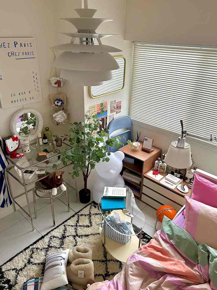 White and natural tone bedroom featuring vanity, mirror, plant, and rug in a cozy compact space