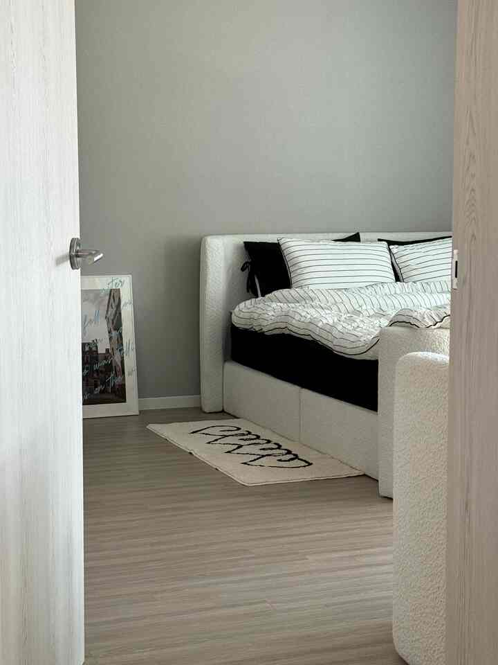 A greige-toned bedroom featuring a modern minimal bed and a small rug with a clean atmosphere