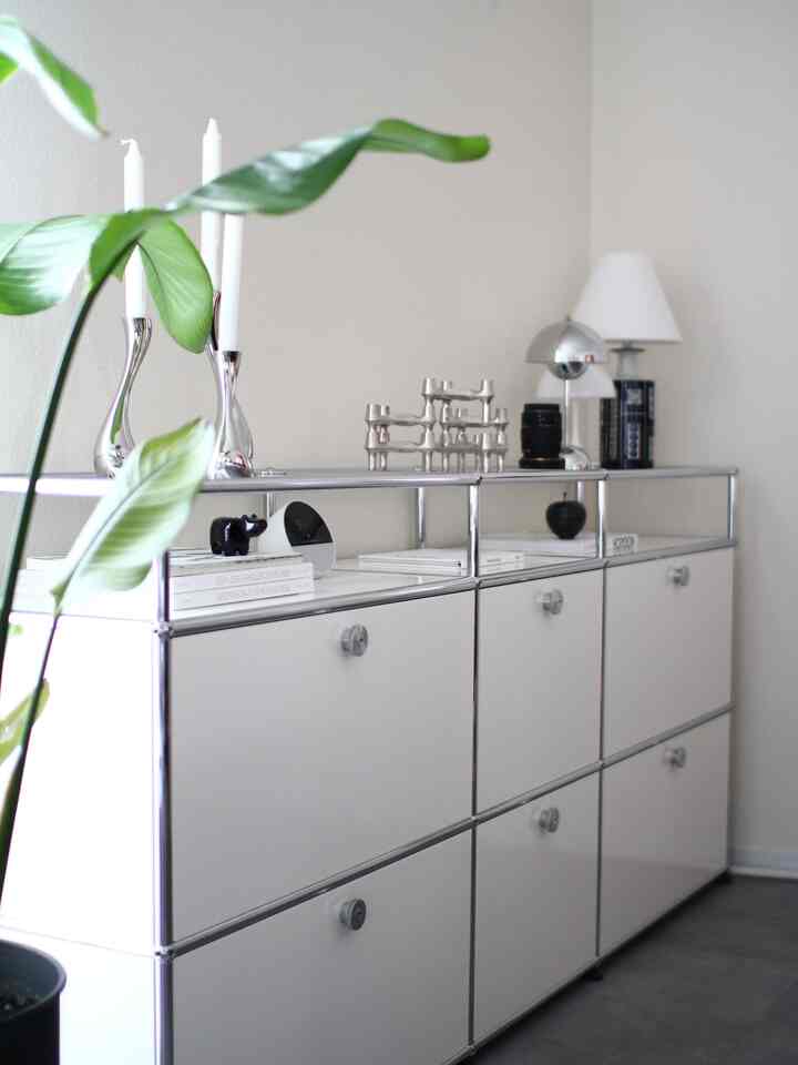 A modern living room in white and silver tones featuring a USM Haller sideboard, candle holders, and table lamps in a minimalist setting