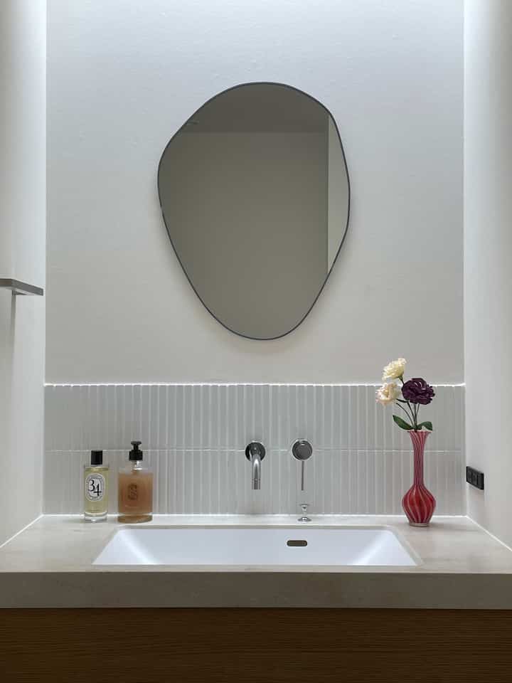 白とベージュのトーンが調和したバスルームの洗面台、特徴的な鏡とミニマルなナチュラルインテリアの空間