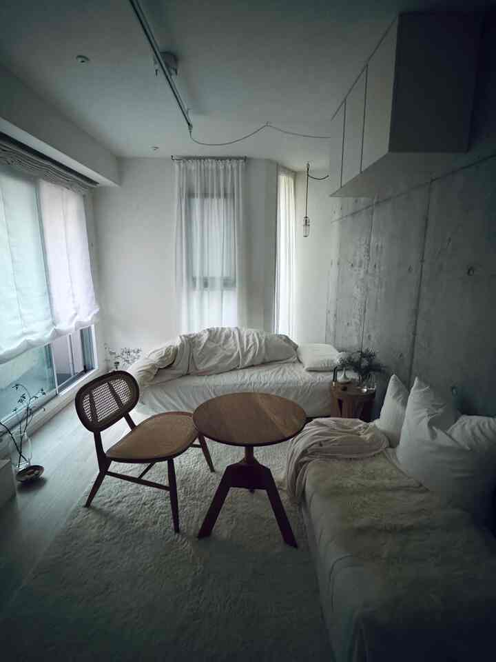 白と茶色の色調の小さなリビング、自然素材の家具とコンクリート壁が調和するミニマルで落ち着いた雰囲気のインテリア