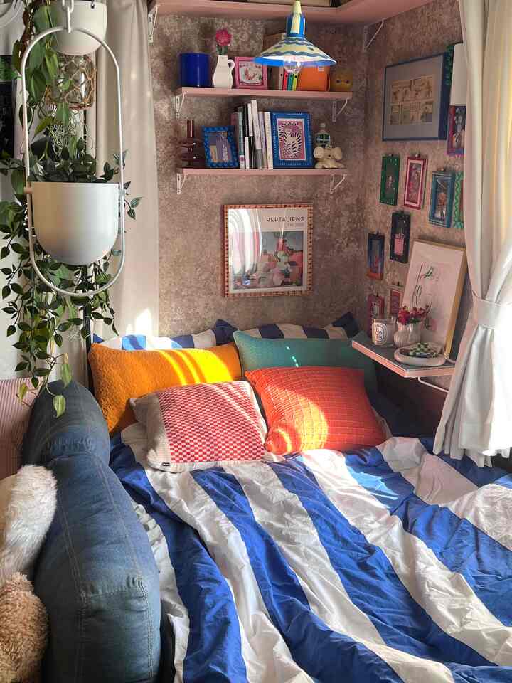 ベージュ調の壁とカラフルなクッション、ブルーとホワイトのストライプの掛け布団カバーが配置された雰囲気のある寝室