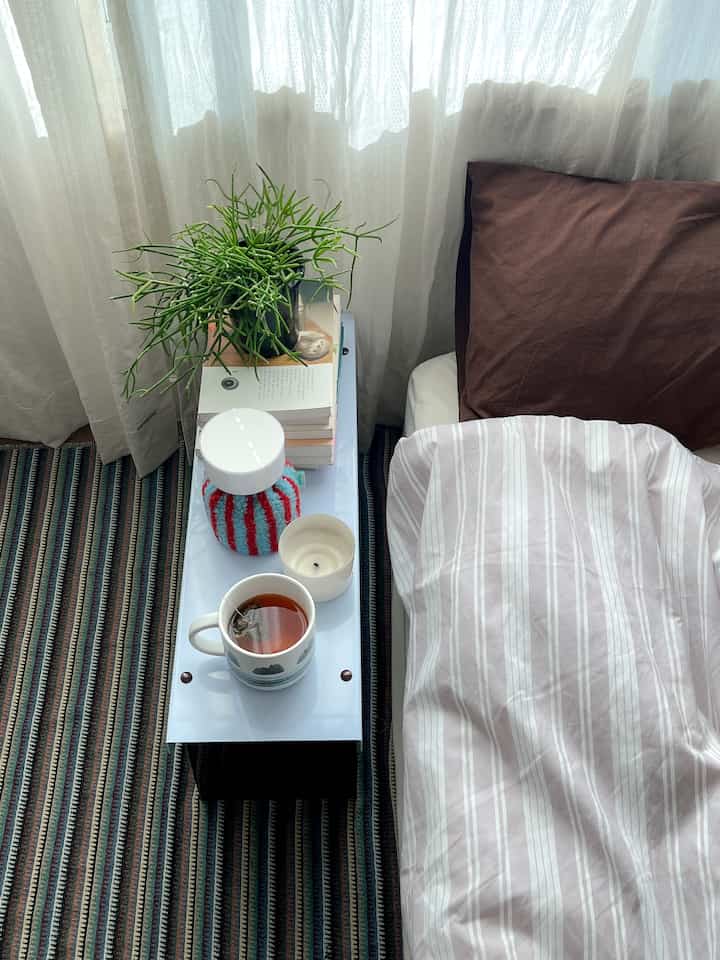 ストライプラグとブラウンピローが配置された寝室、白いシアーカーテンと植物がアクセントの落ち着いた空間