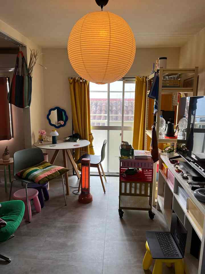 ホワイトとイエローの色調が特徴的な、小さなバルコニー付きアパートのリビング。子供用家具と在宅勤務スペースが配置された温かみのある明るい空間