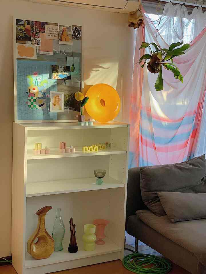 暖かな日差しが差し込む白い本棚とグレーのソファがあるリビング、カラフルな花瓶と植物が印象的なナチュラルなインテリア