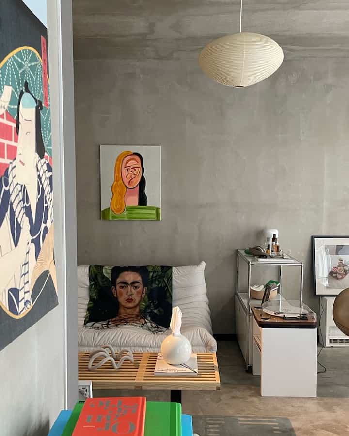 グレーのモノトーンな壁と天井がある1LDKのリビング、白いソファとアート作品、ペンダントライトが配置されたミニマルでインダストリアルな空間