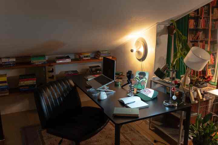 ブラックトーンの狭い屋根裏部屋のホームオフィス、壁棚と壁照明が配置された雰囲気のある作業空間