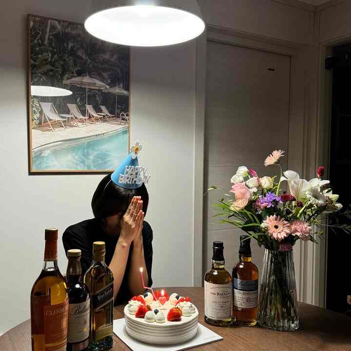 ブラウンの木目調テーブルの上にケーキや酒瓶、花瓶が置かれたダイニングルームで誕生日パーティーを楽しむ様子