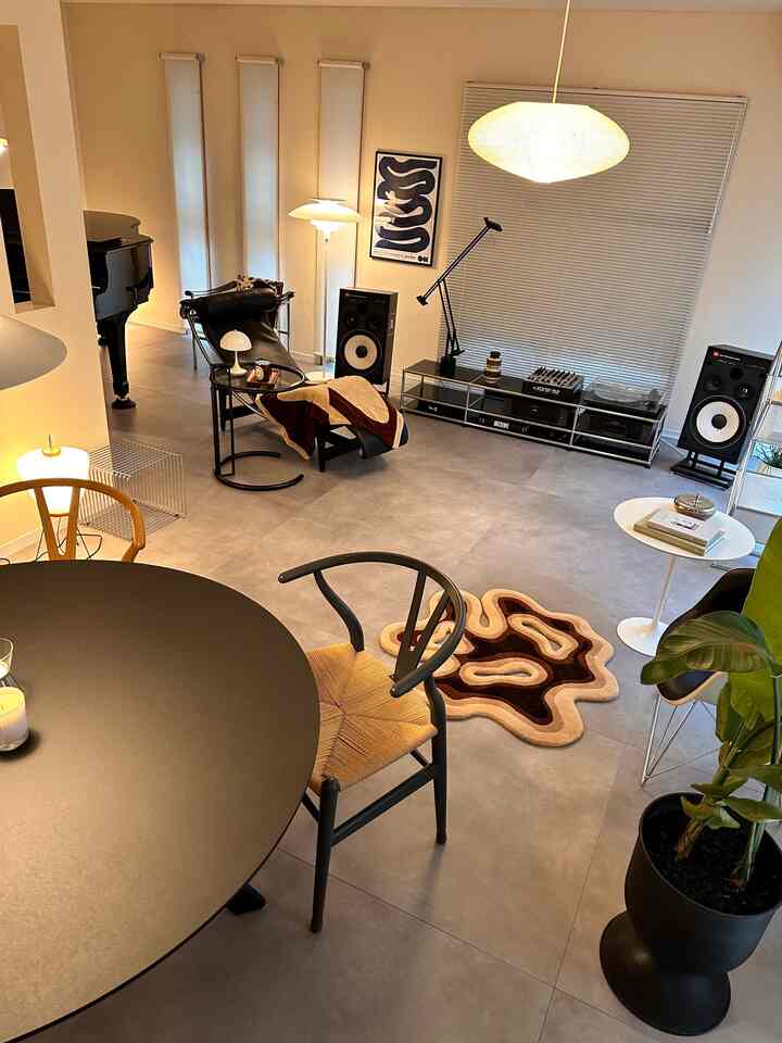 白い壁と天井を背景に、ミッドセンチュリーモダン家具と茶色の抽象的なカーペット、サイドテーブル、照明が調和した広々としたリビングルーム