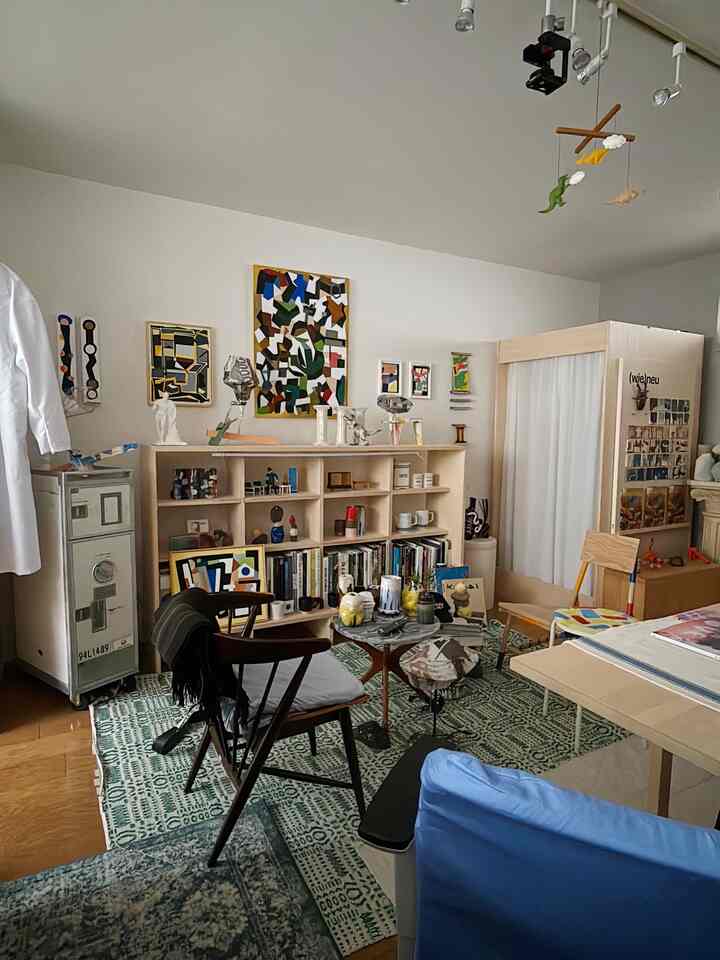 ナチュラルな色調の1LDKリビング、書棚とアームチェア、ラグ、コーヒーテーブルが配置された雰囲気のあるインテリア