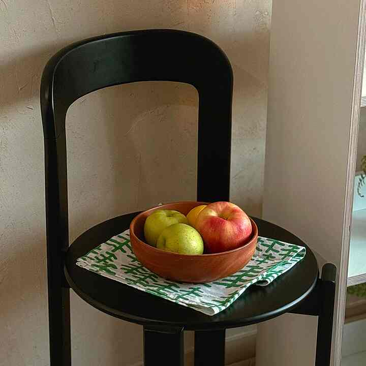 Natural-toned space featuring a black chair with wooden fruit objet and green patterned kitchen cloth on seat