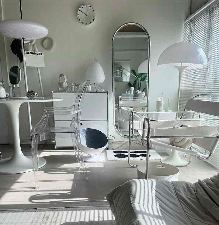 White and black toned living and dining room featuring transparent armchairs and a large floor mirror in a modern, clean interior