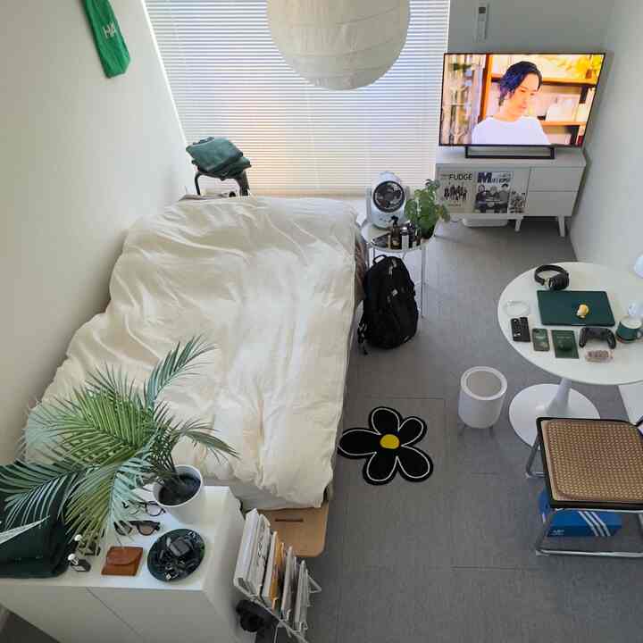 白と緑のトーンが特徴の狭い一人暮らし用寝室、丸いテーブルとラタンのスツール、テレビ台が配置された清潔感のあるインテリア