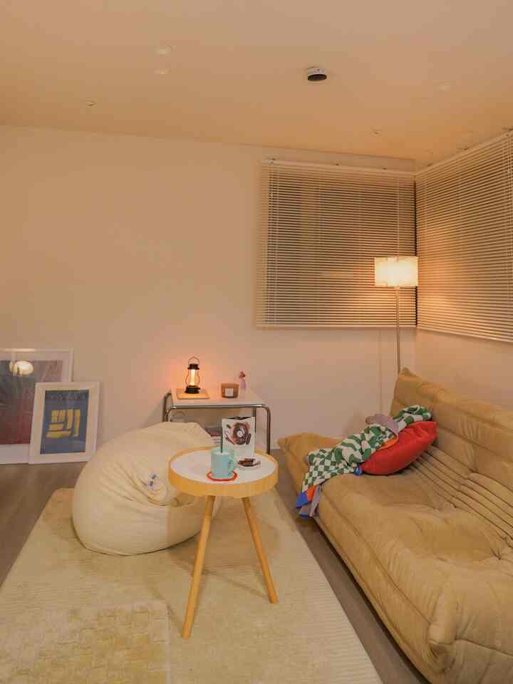 ベージュとクリーム色のナチュラルカラーのリビング、ビーンバッグ、ソファ、サイドテーブル、ムード照明が配置された雰囲気のあるインテリア