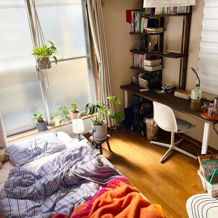 ナチュラルな色調の約20平米の寝室、窓辺とデスク周りに植物が配置された落ち着いたホームオフィス