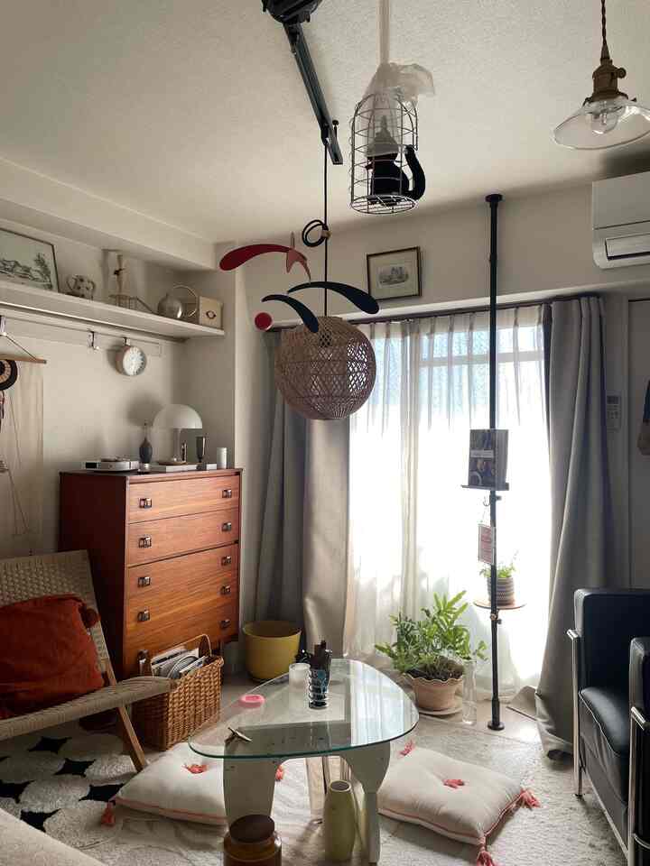 ナチュラルトーンのリビング、ヴィンテージ家具とラタン照明、カーペットや植物が配された雰囲気のある空間