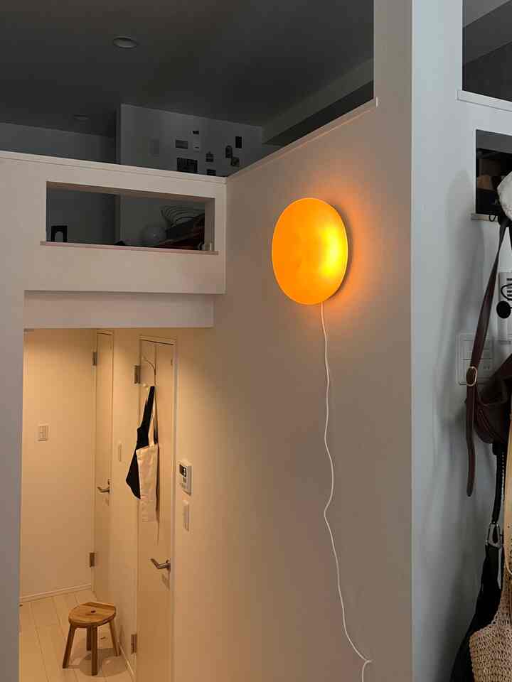 A predominantly white long and narrow loft entrance space featuring a bright orange wall sconce and a wooden stool with natural tones