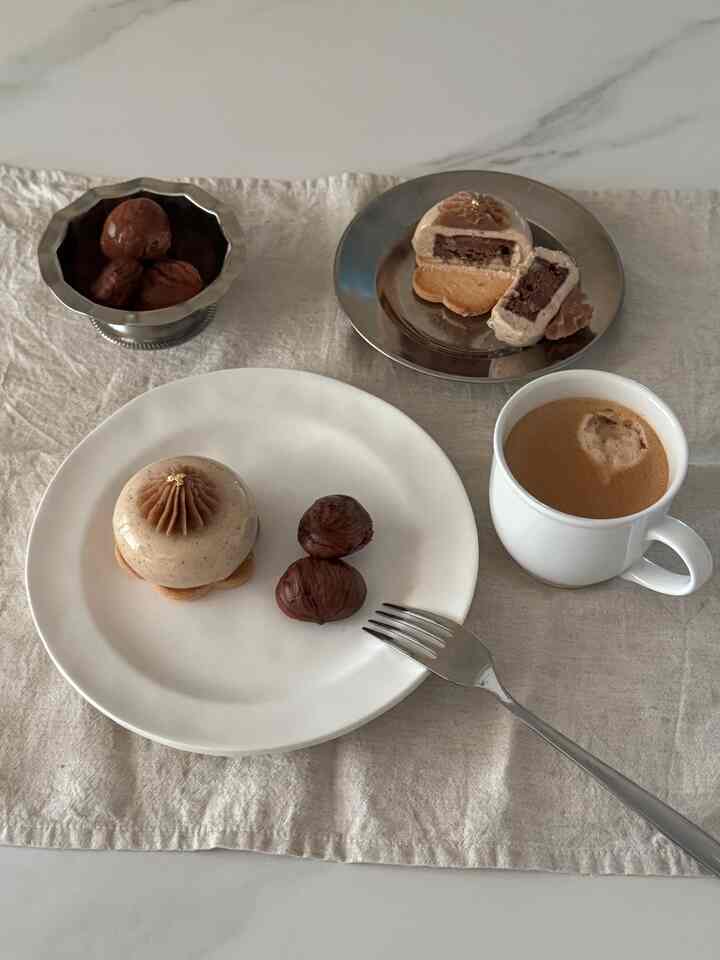 ベージュのリネンテーブルクロスの上に白と銀の皿に秋の栗デザートが置かれた、雰囲気のあるおうちカフェ
