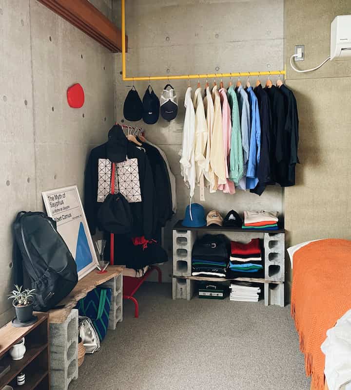 Beige-toned walls and concrete block shelves in a wide room, featuring a yellow clothes rack neatly holding shirts and hats in a walk-in closet space