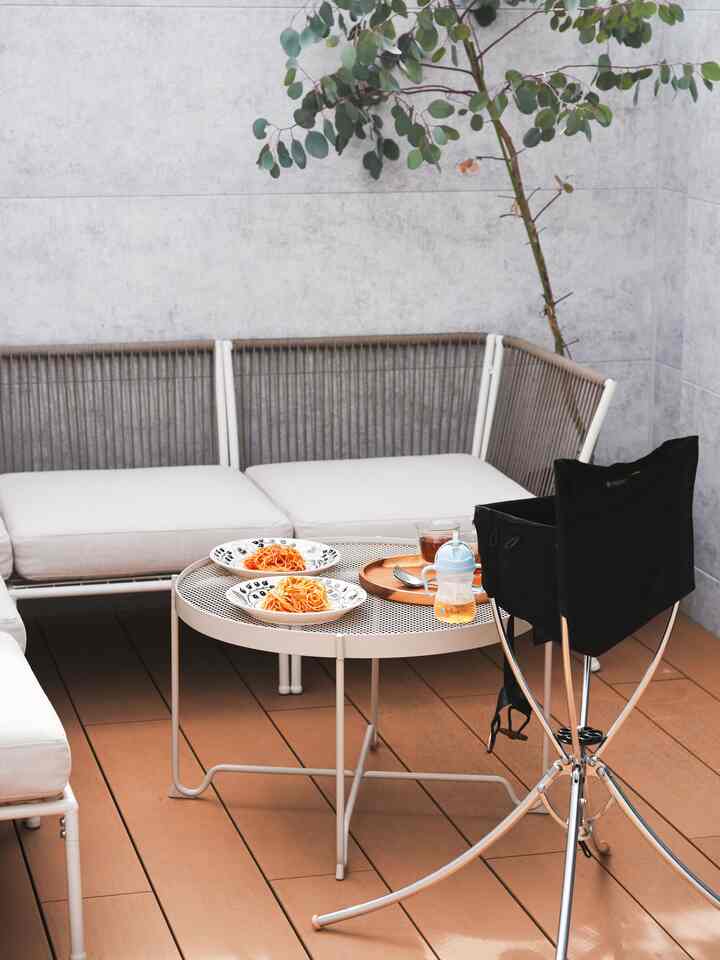 Natural-toned balcony space featuring IKEA outdoor sectional sofa, metal mesh table, and baby chair in a cozy setting