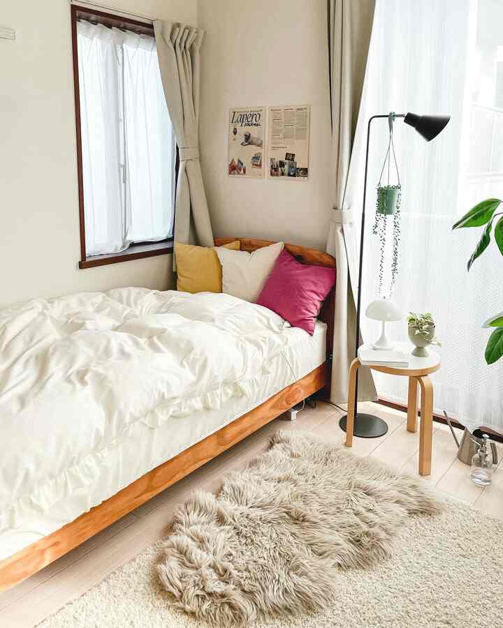 アイボリーとベージュのトーンの寝室、木製ベッドとふわふわのラグが配置された雰囲気のあるインテリア