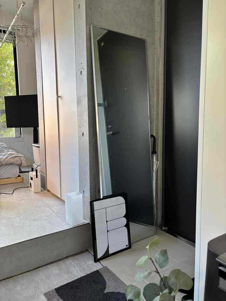 ナチュラルトーンの一人暮らしワンルーム玄関、全身鏡と寝室要素が調和したシンプルモダンなインテリア