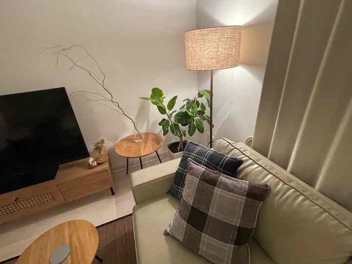 ナチュラルカラーとホワイトトーンのリビング、ベージュのレザーソファとフロアランプ、木製テレビ台とチェック柄クッションが配置された居心地の良い空間