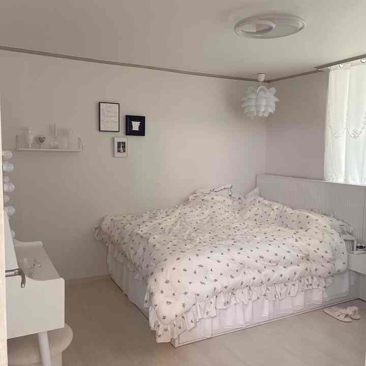 柔らかなホワイトトーンの寝室、フリル付きの模様入り寝具とレースカーテンが雰囲気のある空間を演出