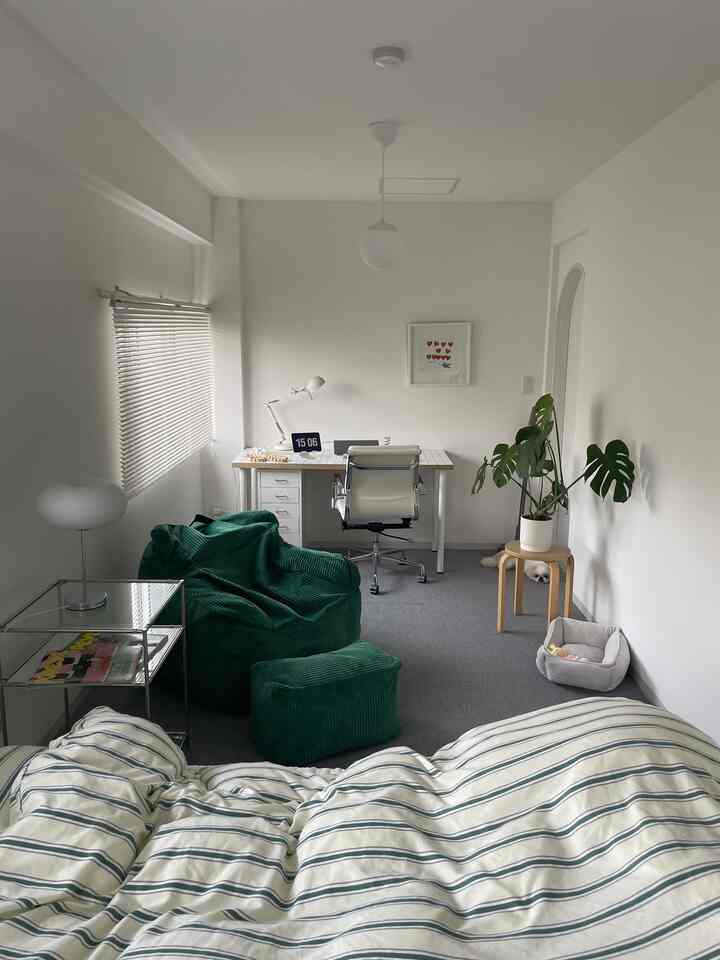 白い壁と家具、緑のビーズクッションと観葉植物が配置された一人暮らしのホームオフィス兼寝室の雰囲気ある空間