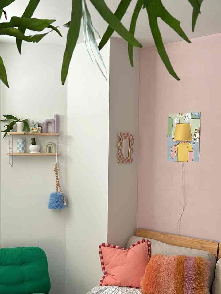 ピンクの壁とグリーンの椅子がある韓国インテリアのリビング、ポスターライトとクッションが温かみのある雰囲気を演出している
