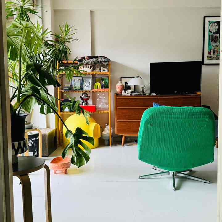 Bright living room with white floor and walls featuring a green armchair and lush plants, creating a cozy atmosphere