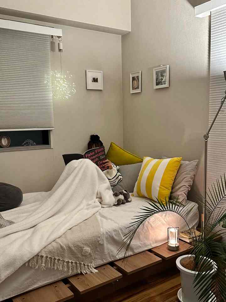 アイボリーと木目調の狭い寝室、クッションとフロアランプが配置された印象的な空間