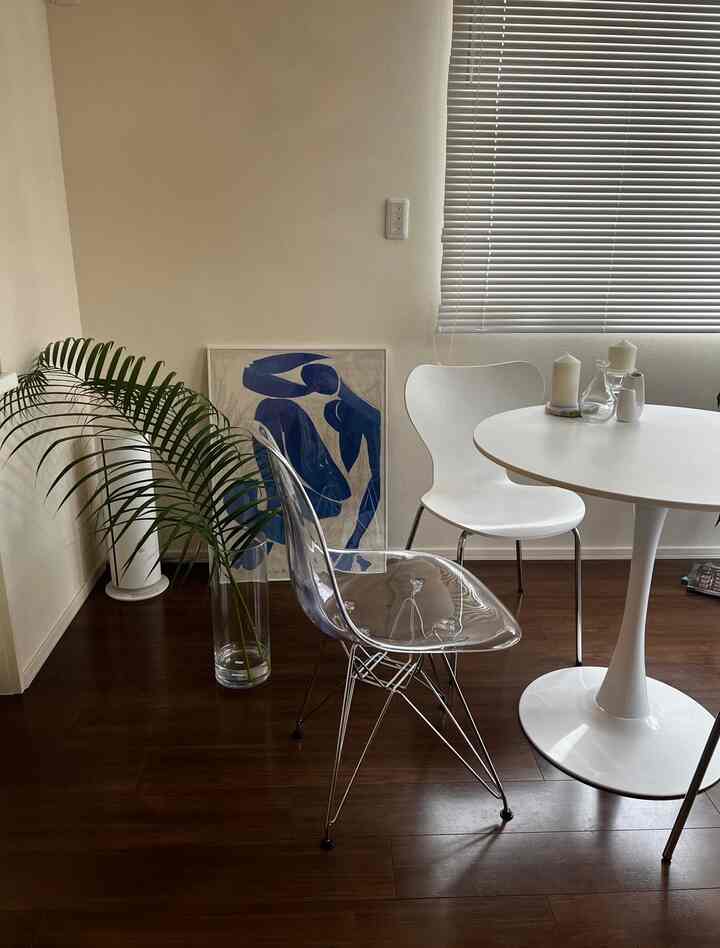 白と透明の家具が配置されたモダンなリビング、アレカヤシの植物とブラインドが調和する印象的な空間