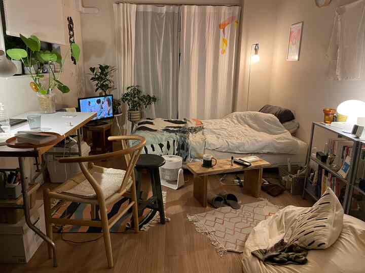 Cozy single household studio in white and brown tones featuring bed, desk, plants in a simple and compact living-bedroom space