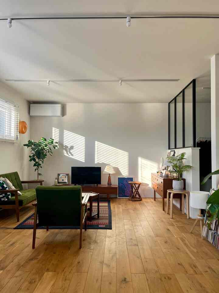 ナチュラルな木目調の床とヴィンテージグリーンのソファが置かれた、自然光が差し込むリビングルーム