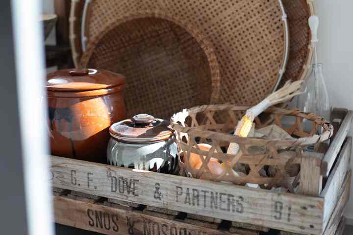 ナチュラルな木目調とヴィンテージスタイルのキッチン、木箱に根菜と伝統的な壺が配置された雰囲気のあるインテリア