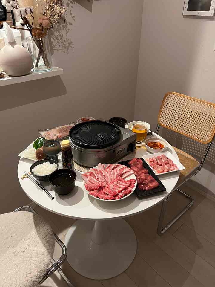 落ち着いた色調のコンパクトな室内に中心の丸テーブルと電気グリル、木目調の椅子が配置された居心地の良いホームパーティー空間