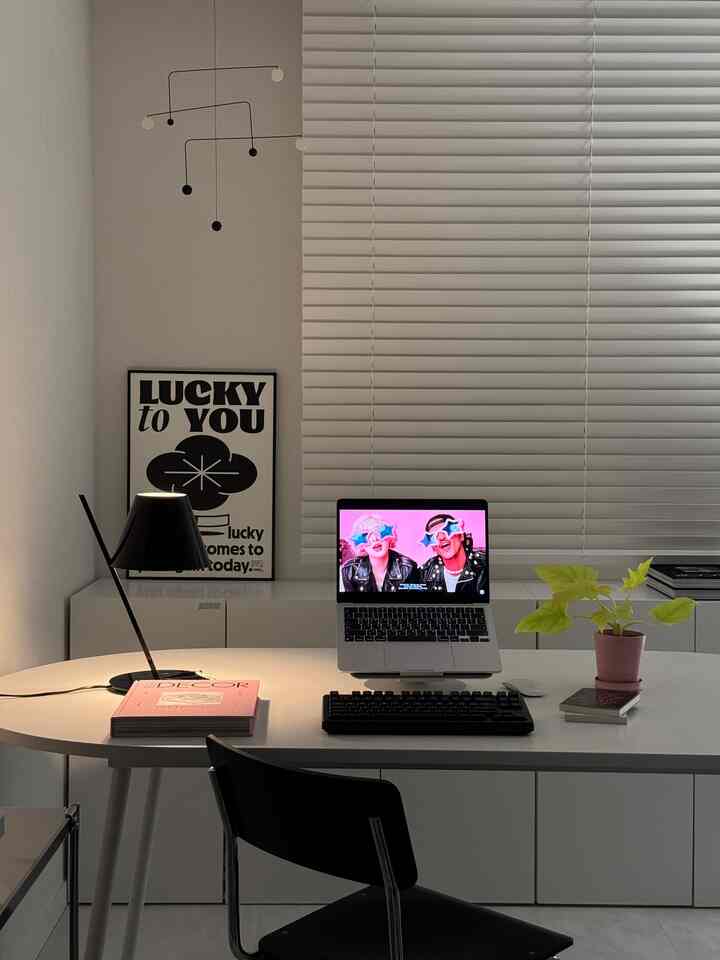 A modern home office in white and black tones featuring a clean desk with mechanical keyboard, laptop, and lamp