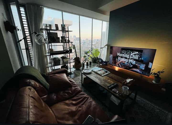 Brown leather sofa and wooden coffee table in a natural-toned living room with large windows creating openness