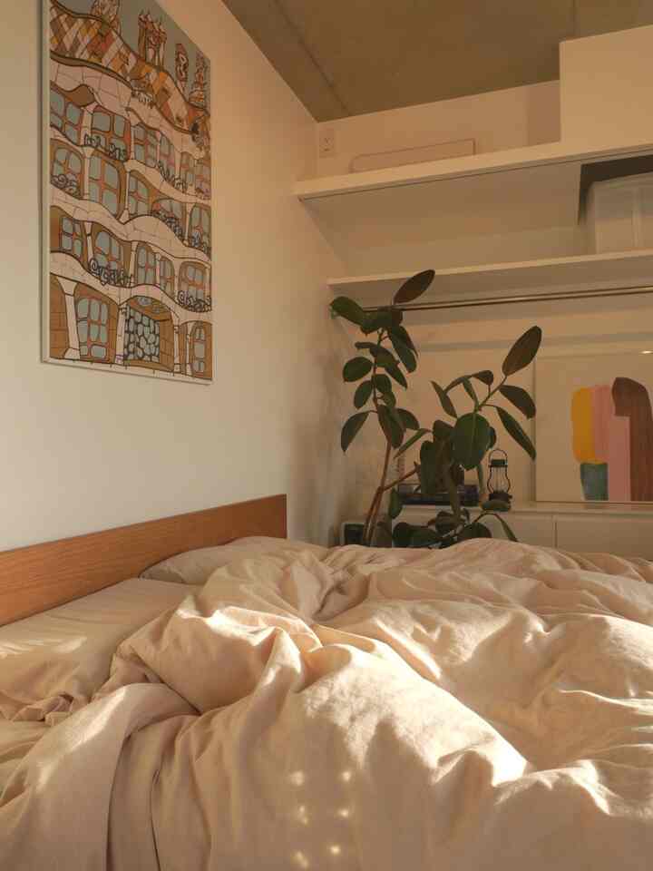 ナチュラルなベージュ調の寝室、木製のベッドフレームと植物が配置された落ち着いた空間