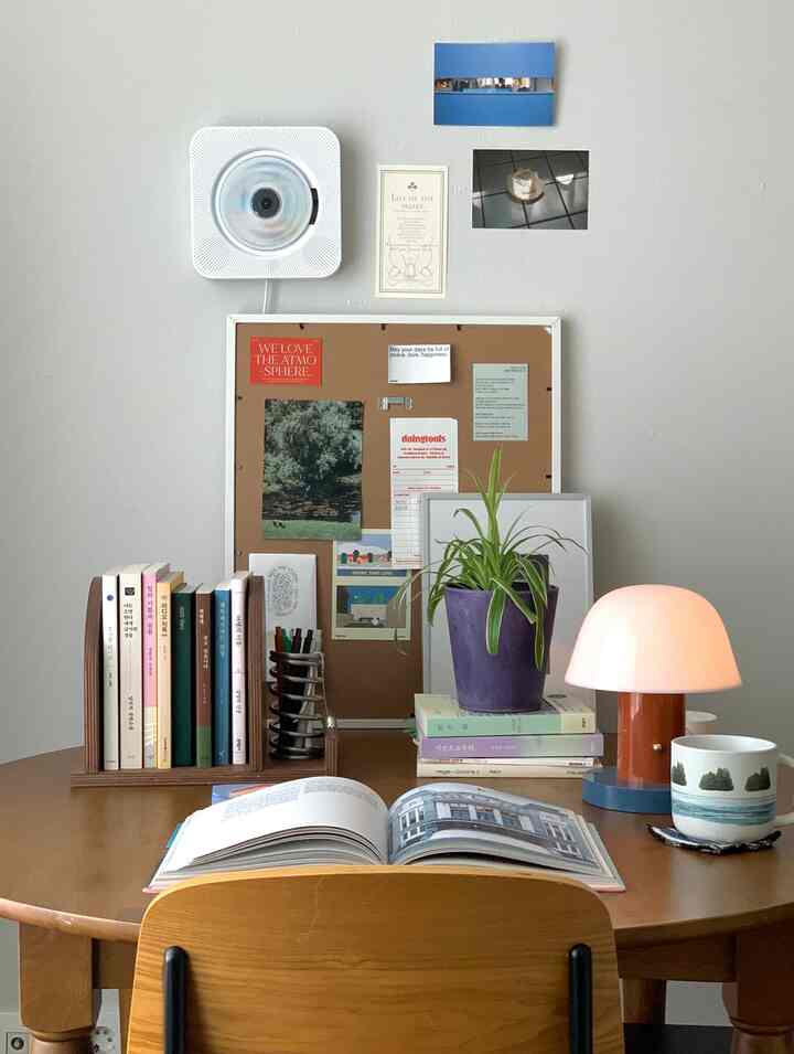 ナチュラルトーンの丸い木製テーブルに本、植物、オレンジ色のテーブルランプが配置された雰囲気のあるホームオフィス空間