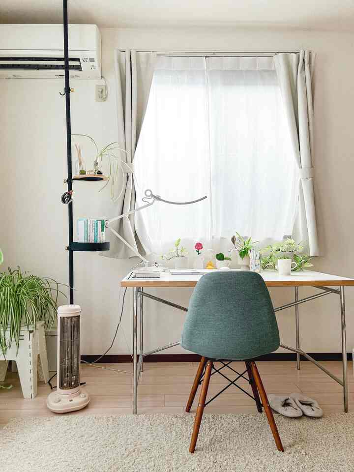 白とナチュラルカラーのホームオフィス、植物や電気ヒーターが配置された明るく居心地の良い作業空間