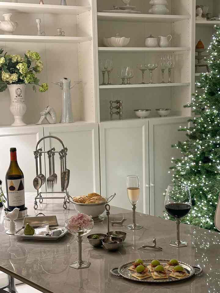 White-toned dining room featuring a marble dining table with wine glasses and a lit Christmas tree, showcasing a modern atmosphere