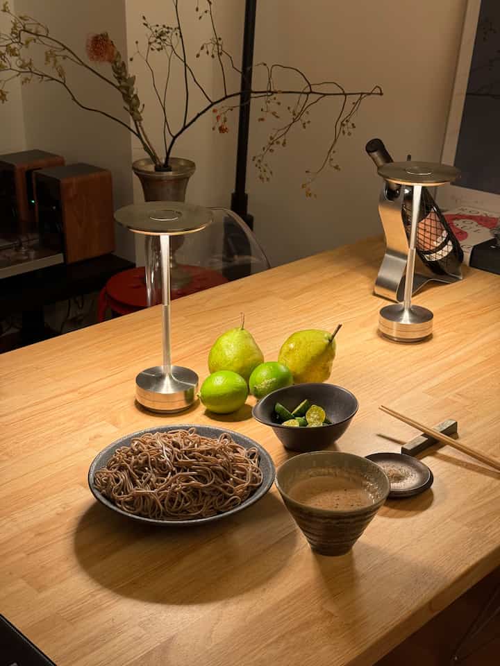 明るい木目調のダイニングテーブルに素朴な陶器の器と蕎麦を配置したナチュラルモダンな一人暮らしの空間